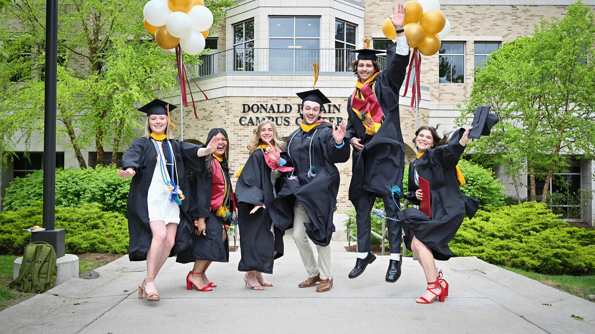 A group of students in commencement regalia jumping in celebration.