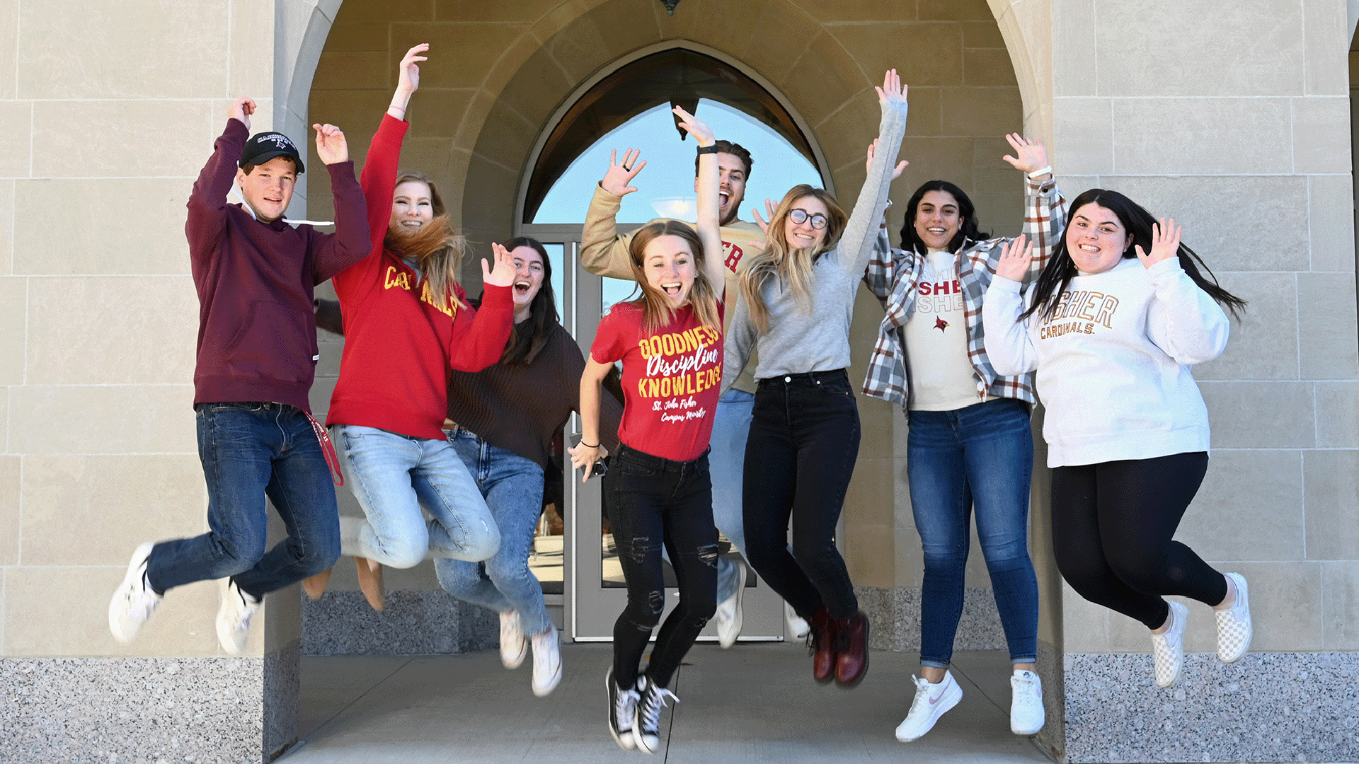 A group of students leap with hands raised in front of Kearney Hall.