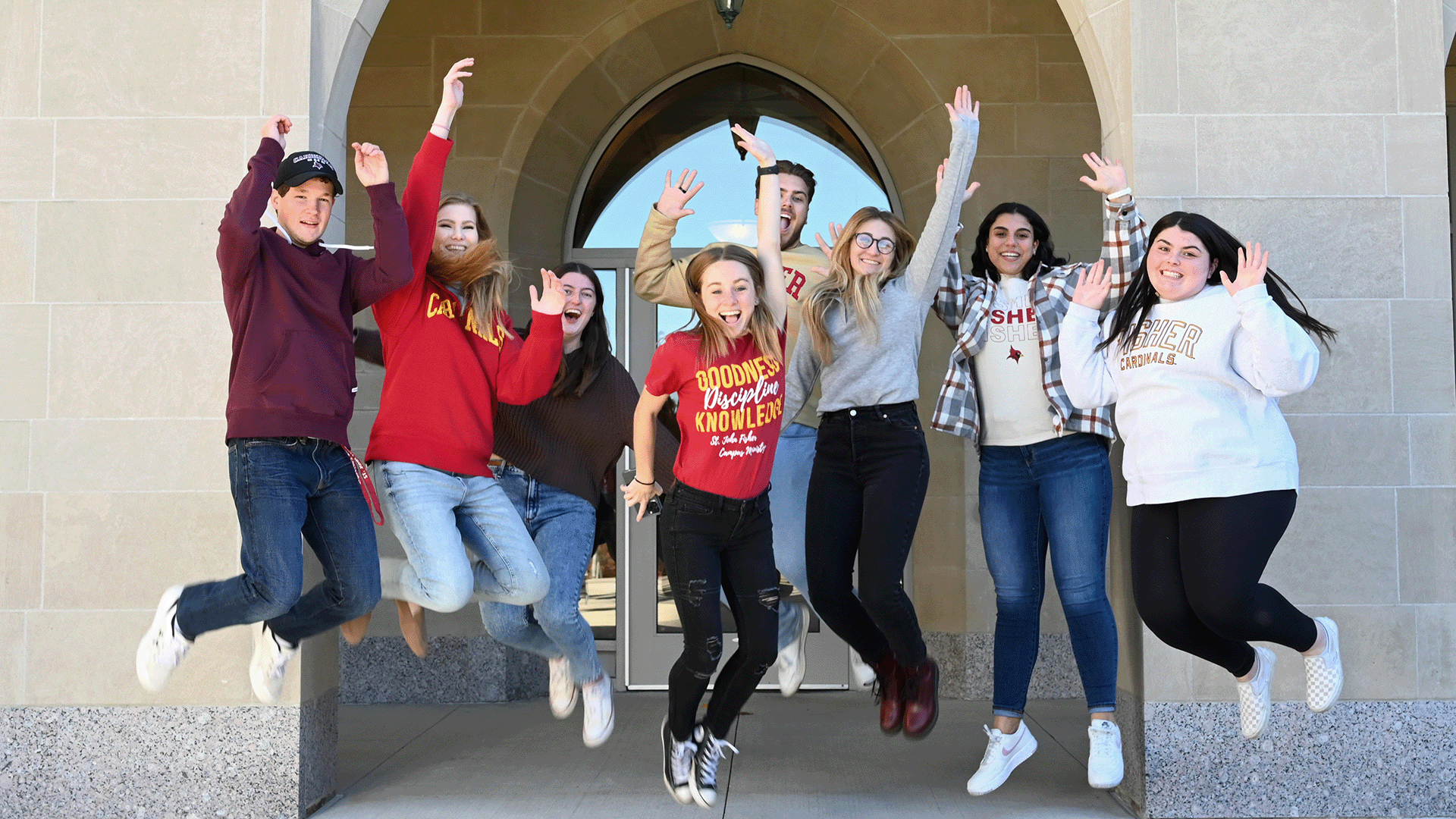 A group of students leap with hands raised in front of Kearney Hall.