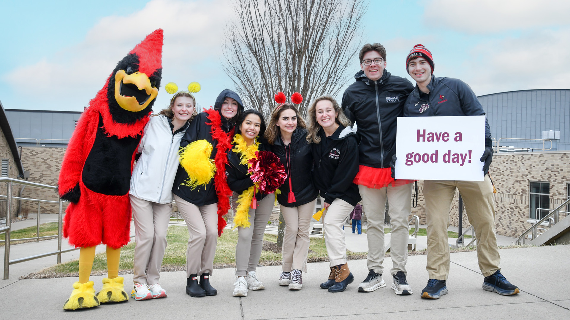 Students welcome visitors to St. John Fisher University for Taste of Fisher holding a sign that says Have a Good Day.