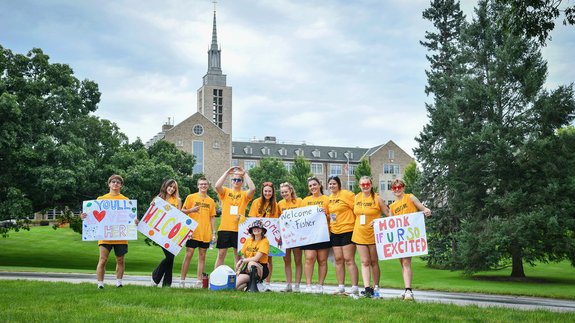 A group of students welcome incoming students to Fisher with welcome signs.