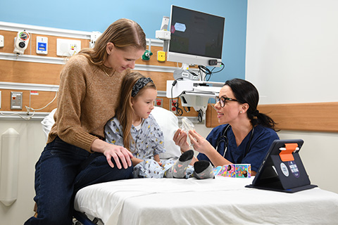A Certified Registered Nurse Anesthetist (CRNA) talks with a patient and her mom with an iPad nearby.