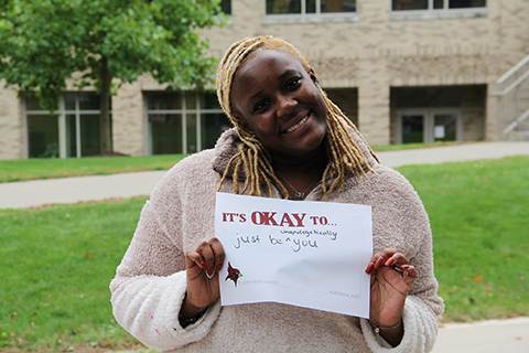 A student holds a sign that reads be unapologetically you.