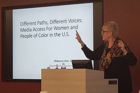 A speaker presents with a screen about women in media.