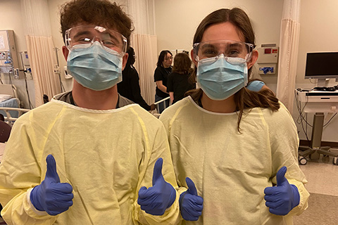 Students in personal protective equipment give two thumbs up during Cardinal Nurse Camp.