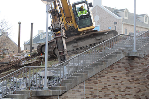 A large construction vehicle demolishes stairs on campus.