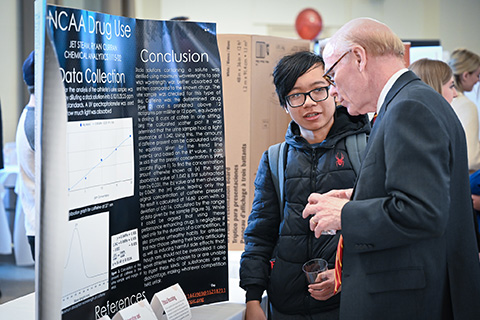Dr. Rooney talks with a student presenting research on a poster at the Fisher Showcase.