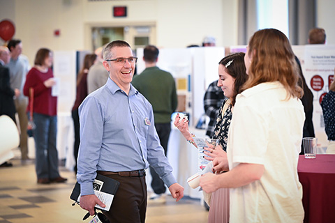 Students and professors discuss student research on display at the Fisher Showcase.