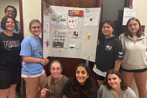 Group of pharmacy camp students standing together in front of a science poster display.