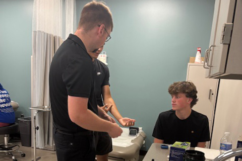 Two students are seen speaking with an instructor in a clinical room.
