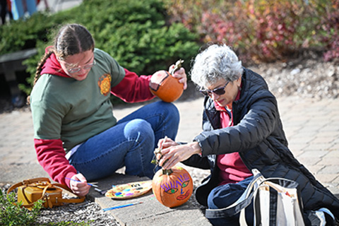 A student paints a pumpkin with a family member at Fisher's Family Weekend.