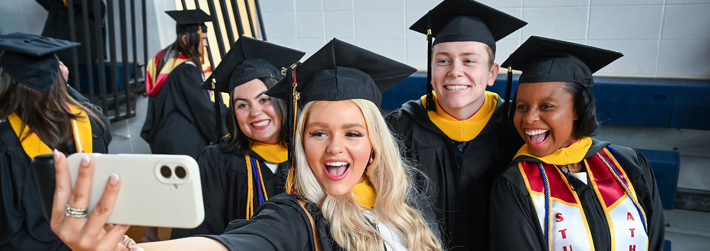 Students in commencement regalia taking a selfie.