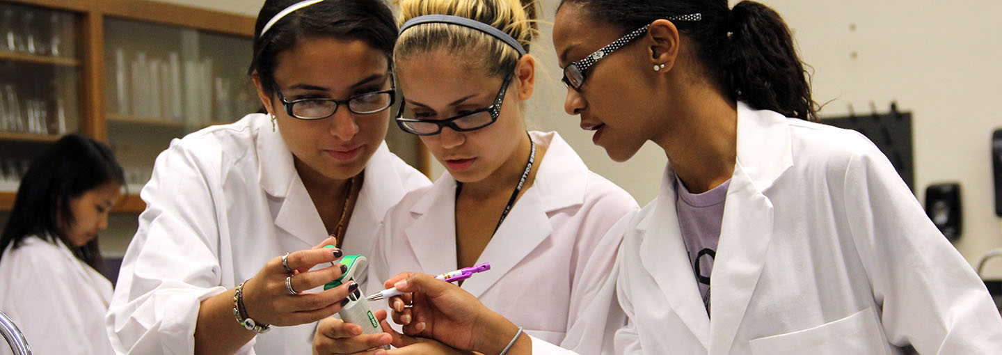 Three students in lab coats in a classroom