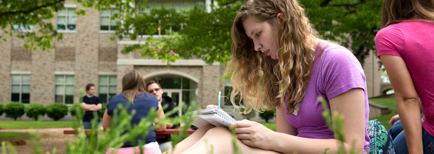 Student taking notes while sitting outside.