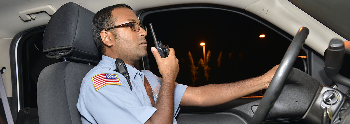 Security officer with radio in hand in patrol car.