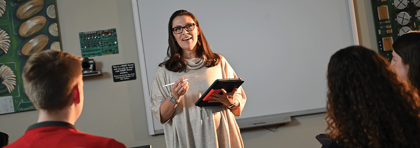 An educator teaches from an iPad in front of a class.