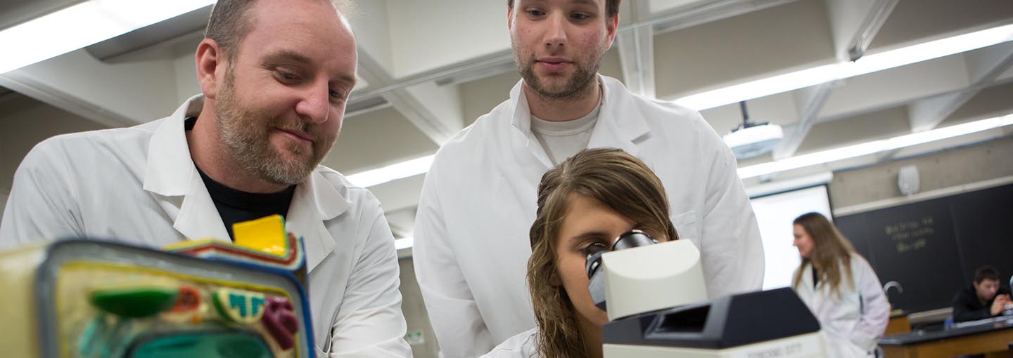 Biology faculty and two students using a microscope