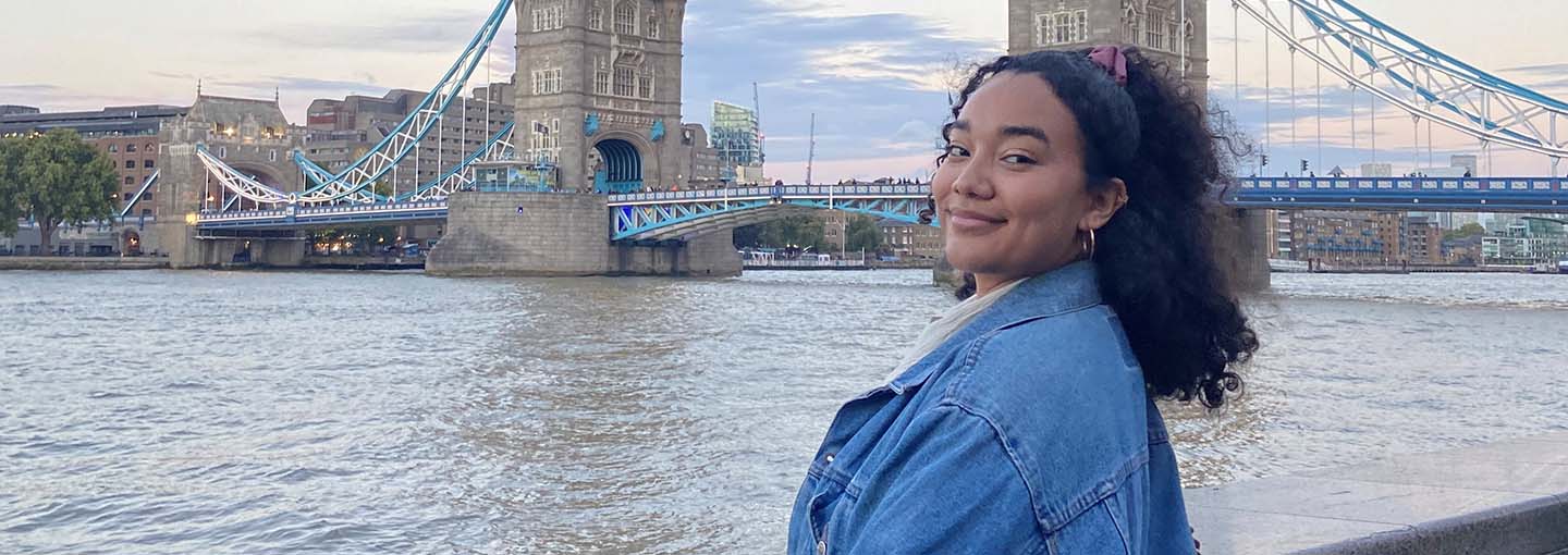 A student stands near a river and iconic bridge during her study abroad trip.