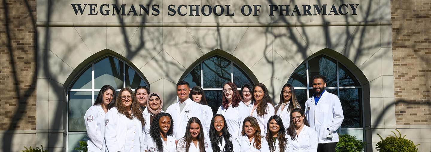 Pharmacy students in white coats in front of Wegmans School of Pharmacy.