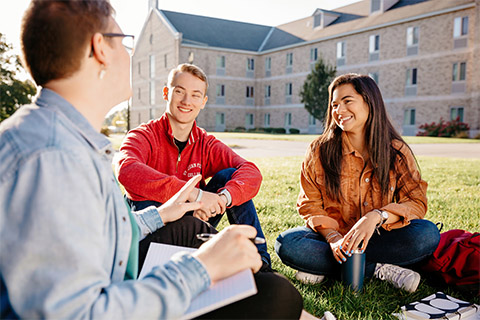 A group of students sits outside with a professor.