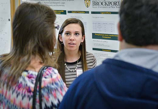 Student speaking to two adults in front of a scientific poster.