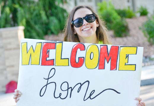 Female student holding Welcome Home sign.