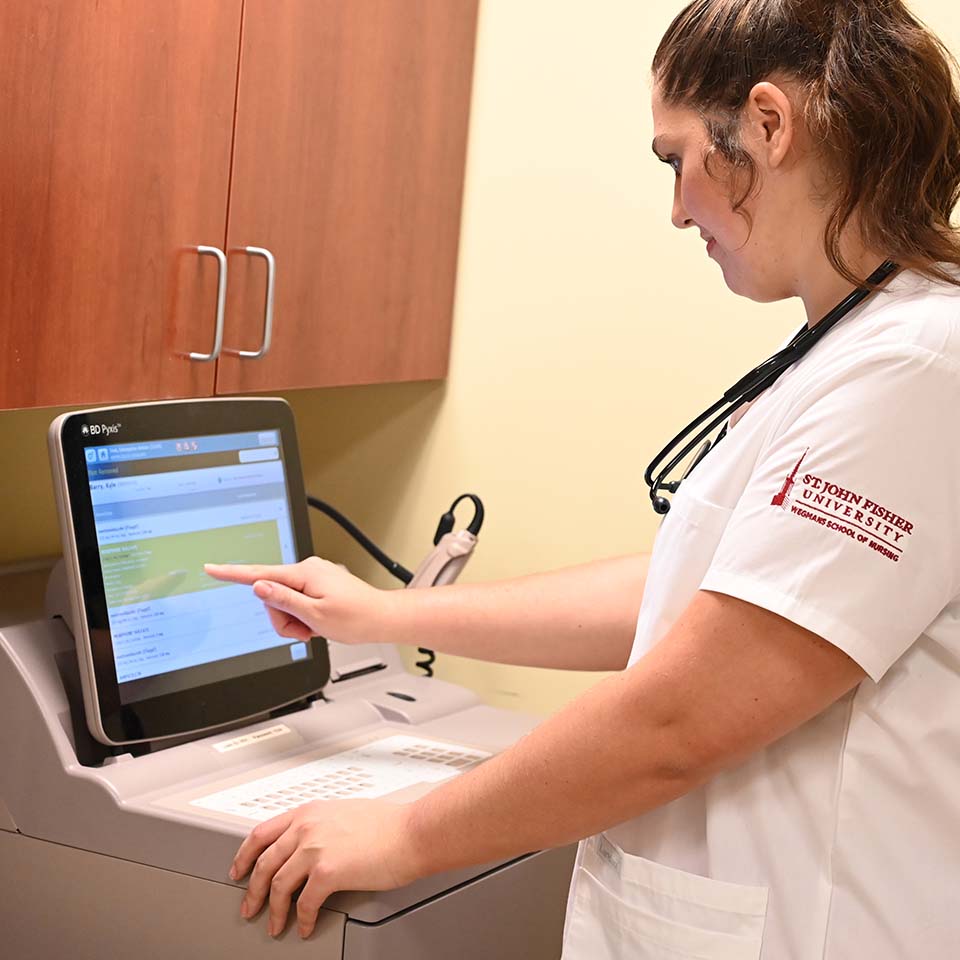A nursing student uses a computer to release medication on a medicine cart.