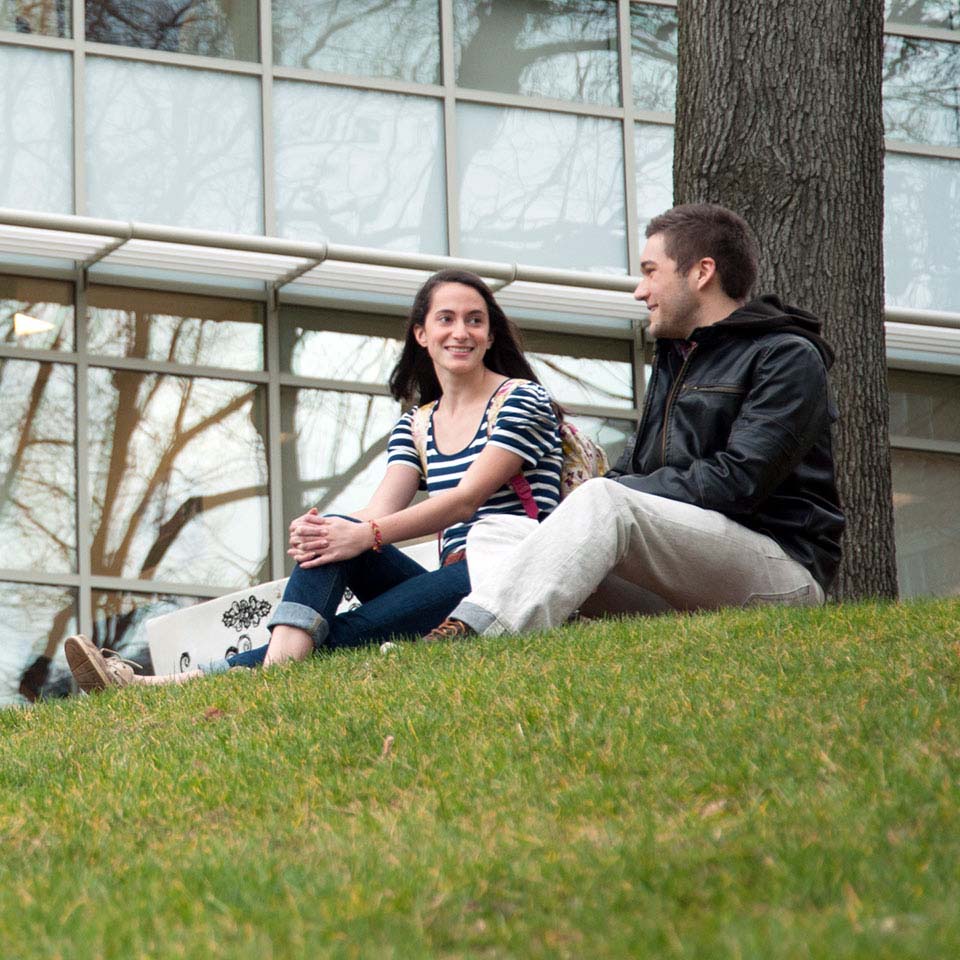 Male and female students talk on grassy hill.