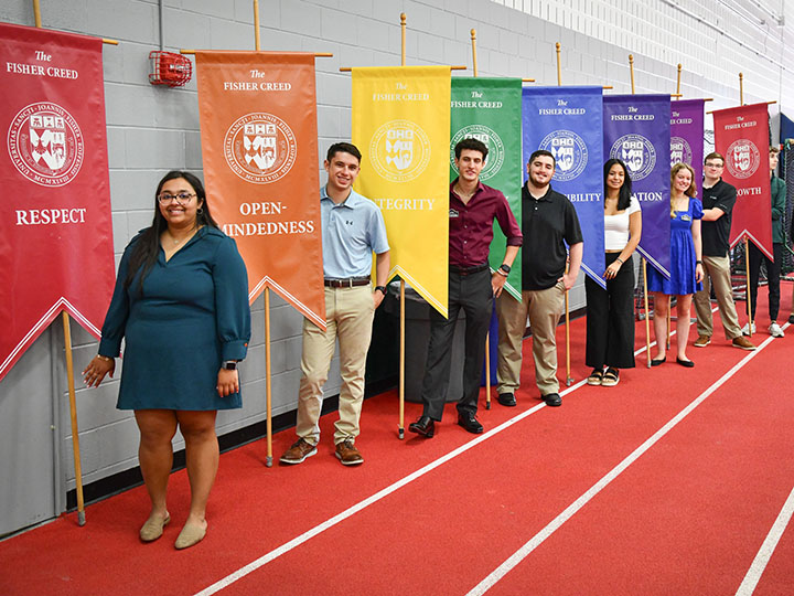 Students standing with banners for the pillars of the Fisher Creed during Matriculation.
